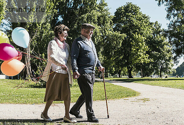 Happy senior couple walking with balloons on sunny day