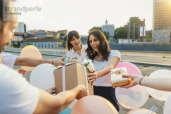 Happy woman with friends giving gifts and celebrating birthday together at sunset