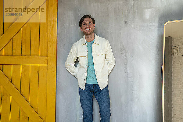 Happy man with hands behind back leaning on gray wall