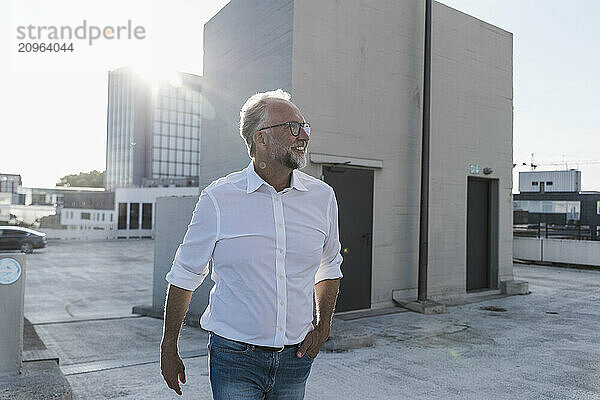 Happy mature man with hand in pocket walking on terrace