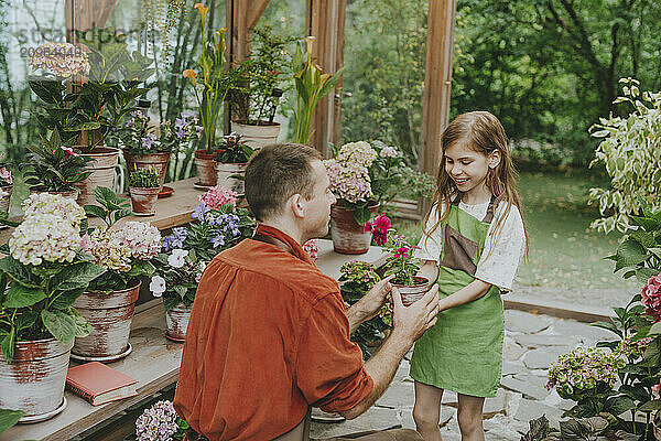 Father giving potted plant to daughter in greenhouse