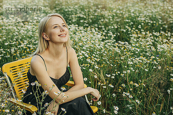 Smiling woman sitting on chair in meadow