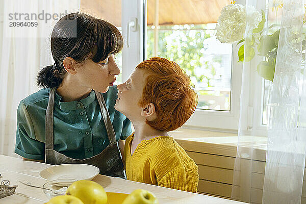 Mother kissing son near window in kitchen