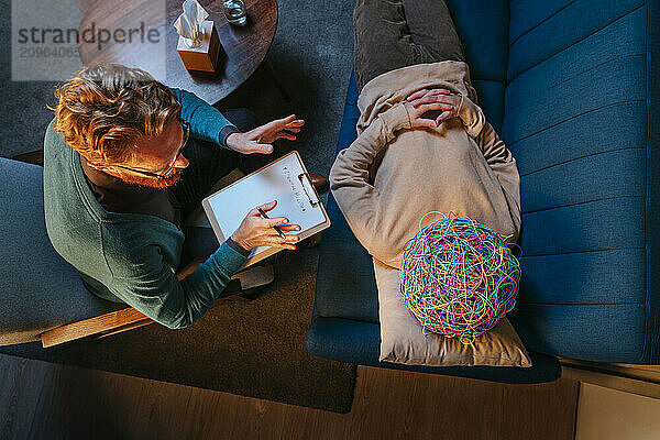 Psychotherapist advising patient with chaotic mask lying down on sofa