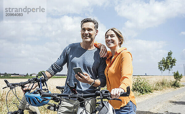 Happy man holding smart phone standing with woman holding bicycle