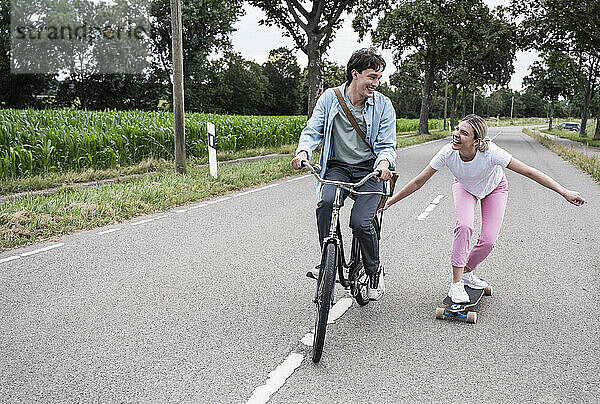 Cheerful woman skateboarding with boyfriend riding bicycle on road