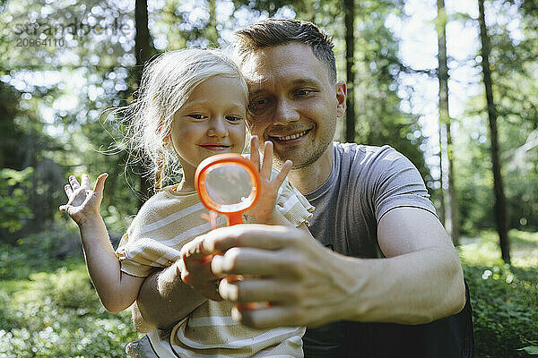 Father and daughter looking through magnifying glass in forest