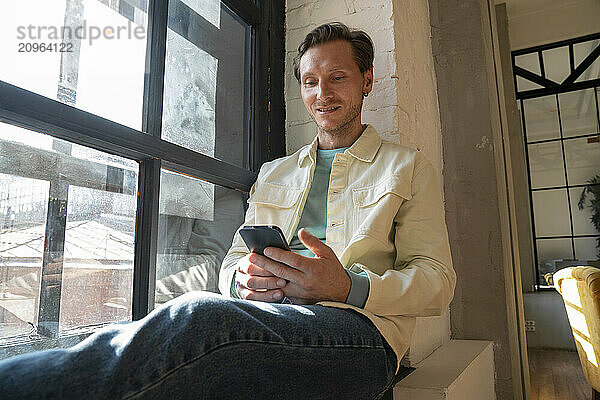 Smiling man using mobile phone in home