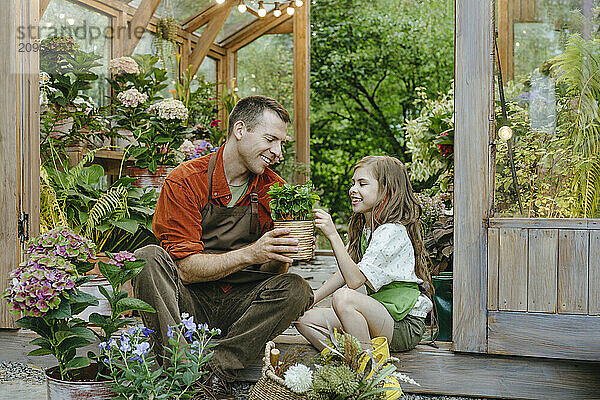 Happy girl examining potted plant with father sitting in greenhouse