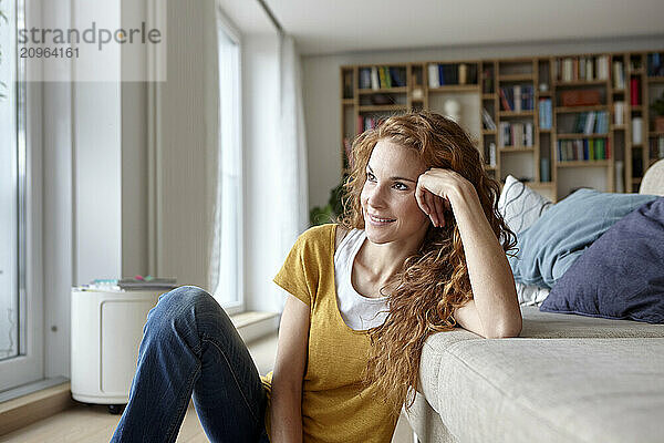 Contemplative woman leaning on elbow and sitting near sofa at home