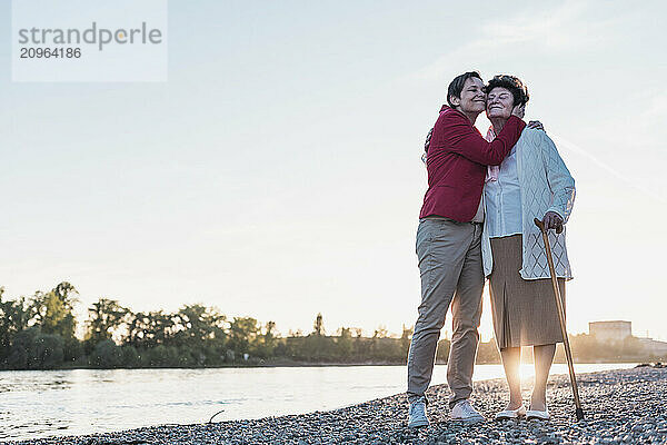 Happy daughter embracing mother near river at sunset