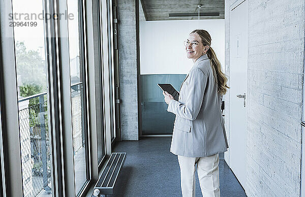 Happy businesswoman walking with tablet PC in corridor