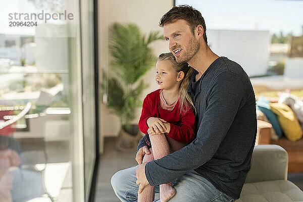 Smiling father and daughter looking out of window sitting at home