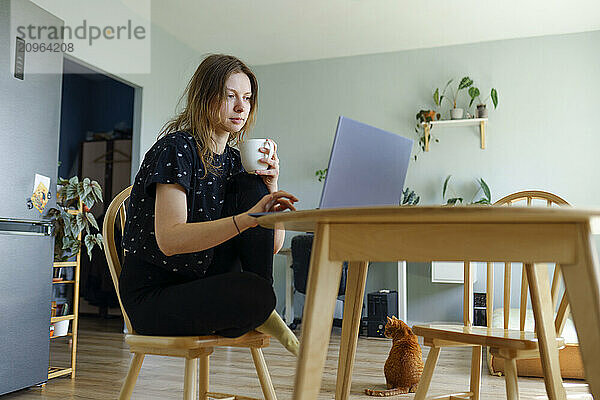 Freelancer holding coffee cup and working on laptop at home