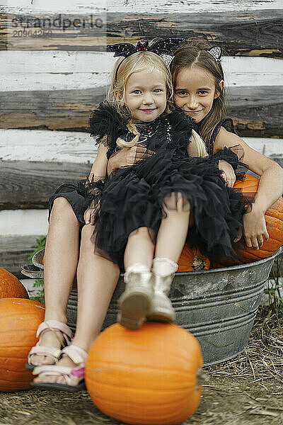 Smiling girl sitting with sister over pumpkins in bucket