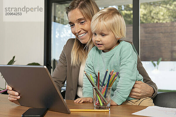 Happy freelance mother using tablet PC with son at home