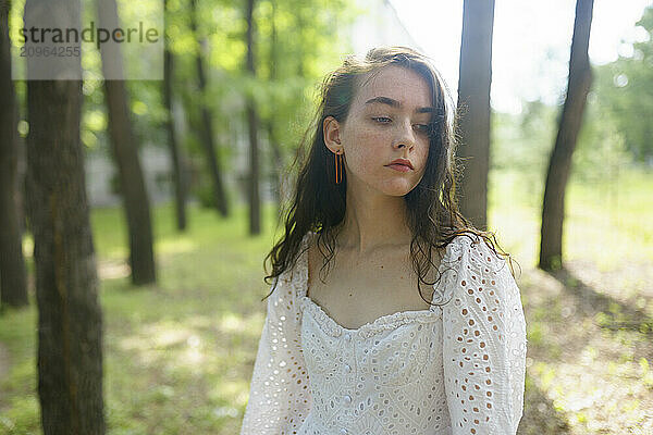 Thoughtful girl in white dress at forest