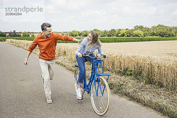 Happy woman riding bicycle with man running on road