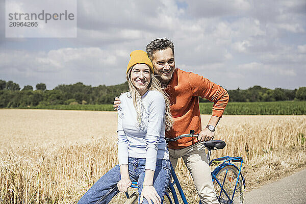 Happy woman sitting on bicycle with man at field