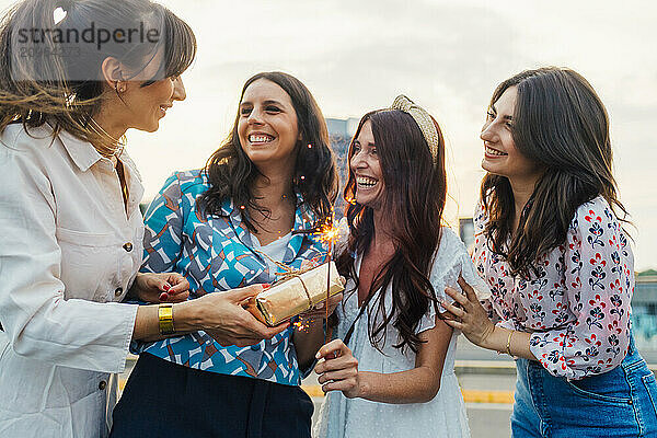 Happy woman giving gift to friend holding sparkler and enjoying together at sunset