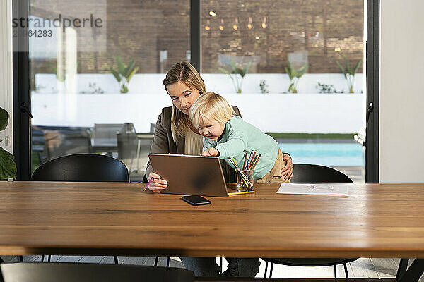 Working mother with son using tablet PC sitting at table in home