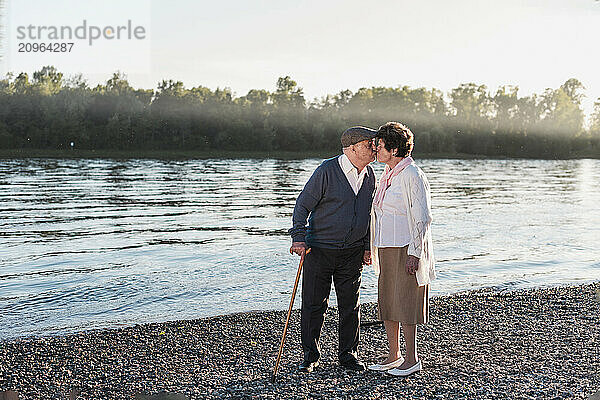 Senior couple kissing and standing together near river