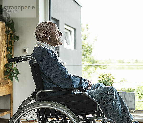 Thoughtful senior man sitting in wheelchair and looking through window