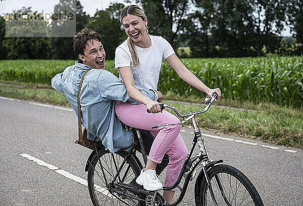 Playful man sitting behind girlfriend riding bicycle on road