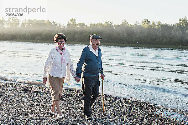 Happy senior couple holding hands and walking at riverbank