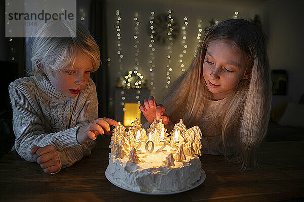 Siblings sitting with illuminated Christmas cake at home