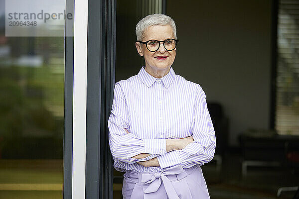 Confident senior woman leaning against balcony door at home