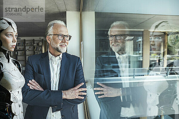 Smiling businessman with arms crossed looking through glass window at office