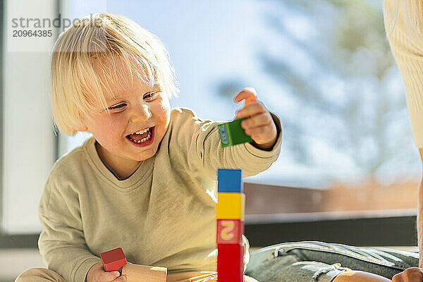 Happy boy with blond hair playing with building bricks at home