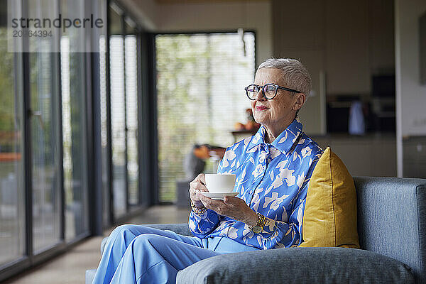 Senior woman sitting on couch at home with cup of coffee