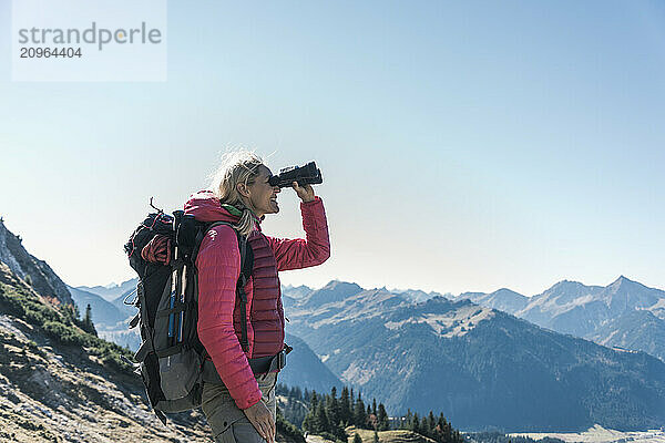 Mature woman with backpack looking through binocular on mountain