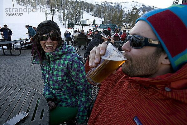 Friends in ski gear socialize and enjoy a beer on the deck on a sunny day on the mountain.