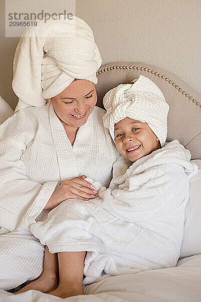 Mother and daughter smiling together sitting in bed with white robes