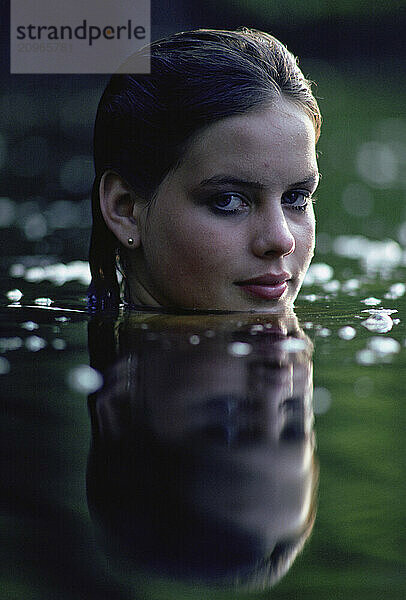 A portrait of teenage girl in the calm waters of a pond.