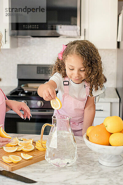 Little girl putting a lemon slice in a pitchen with lemons around her