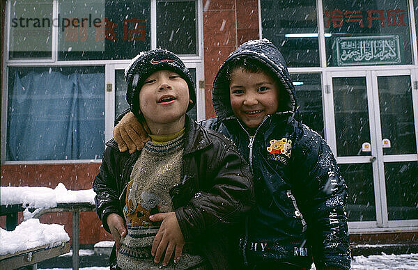 Two Chinese Uygur children play together outside in the snow.