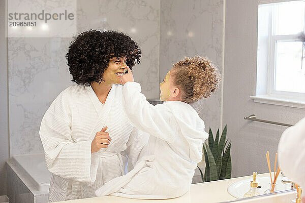 Little sister puts her finger on big sisters nose in the bathroom