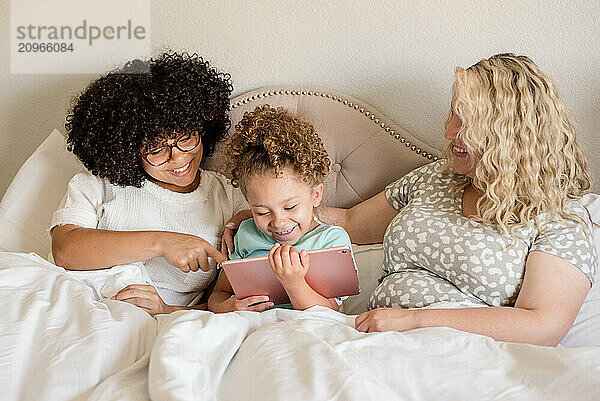 Little girl holding a tablet with mother and big sister