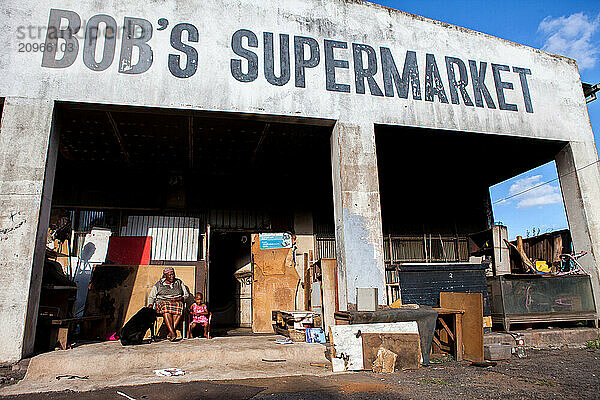 Woman  child and dog sit outside an abandoned gold mining grocery store.