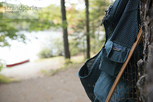 A Fly Fishing Vest And Net Hanging On A Tree Along A River In Maine