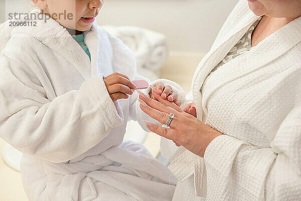 Little daughter is filing mothers nails with white robes