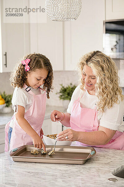 Mother and daughter placing cookies on a cookie sheet in the kitchen