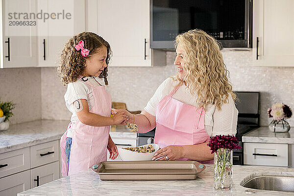 Mother and daughter holding a spoon in the kitchen with cookie dough