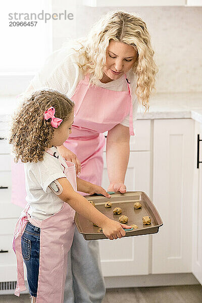 Daughter holding a baking sheet with cookie dough with mother helping