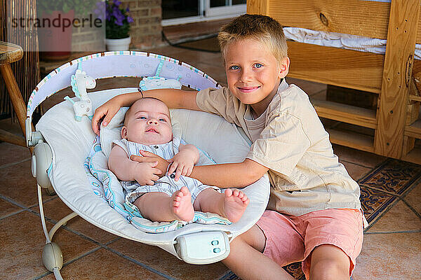 Big brother hugging baby brother relaxing in swing