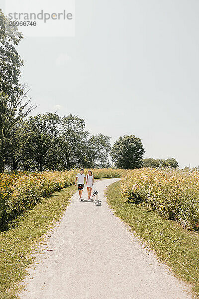 Young couple walking with dog on path lined with wildflowers